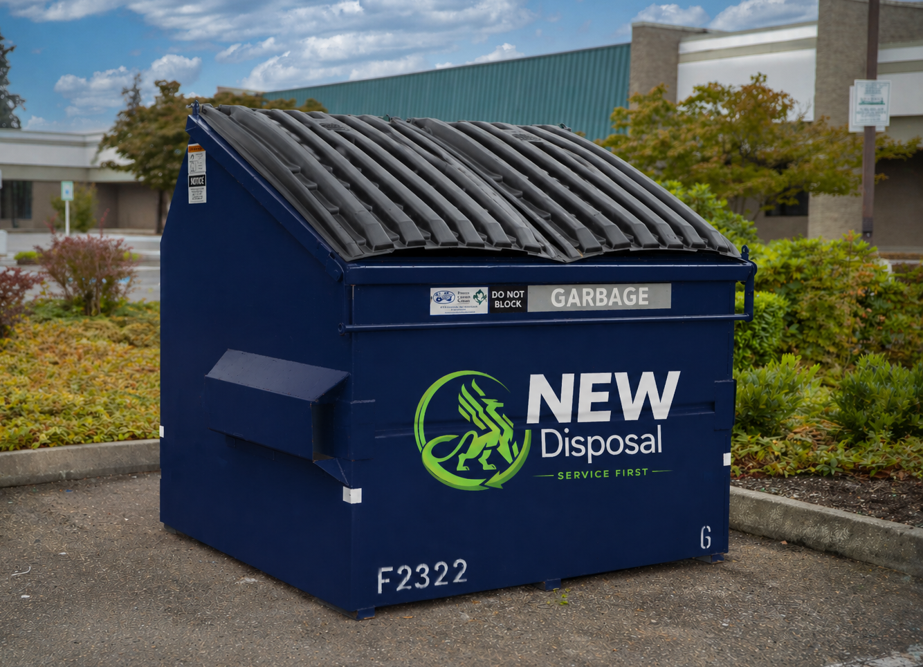 A navy blue commercial front-load dumpster with a black ribbed lid and NEW Disposal branding, sitting in a landscaped parking area.