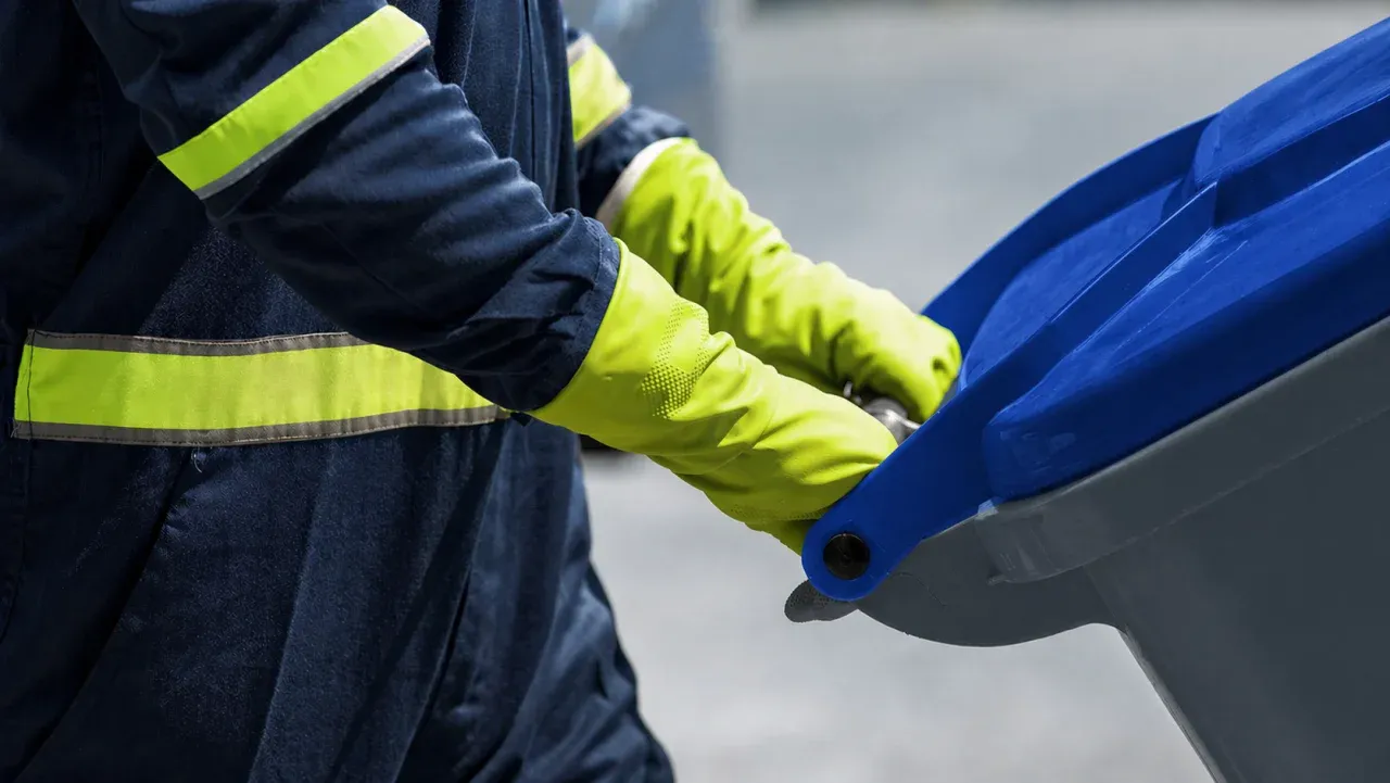 A NEW Disposal team member in safety gear handles a residential cart curbside.